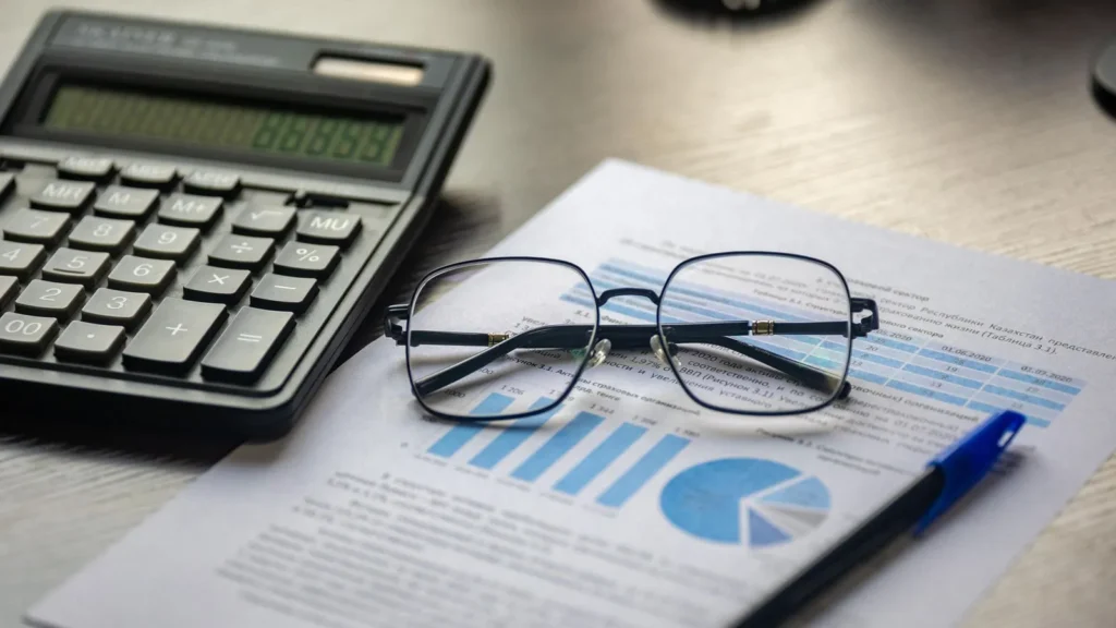 Calculadora, lentes y documentos financieros sobre un escritorio