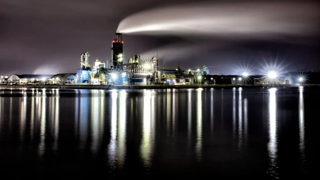Complejo industrial iluminado de noche, reflejado en el agua
