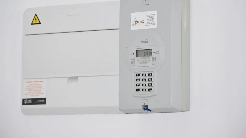Medidor eléctrico digital junto a un tablero en una pared blanca