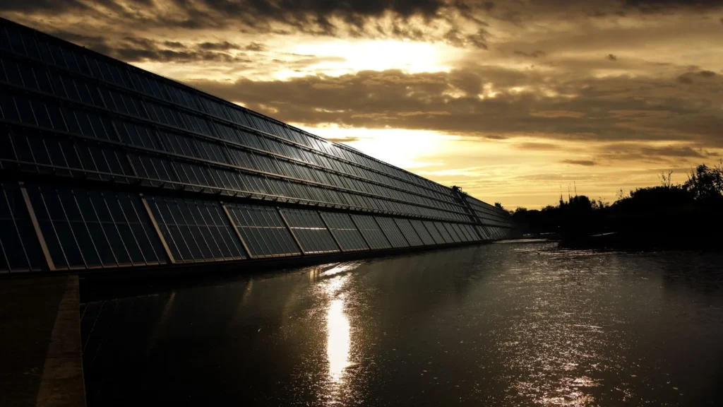 Hilera de paneles solares al atardecer, reflejada en el agua