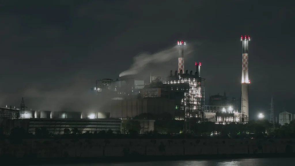 Planta industrial iluminada de noche junto a un río